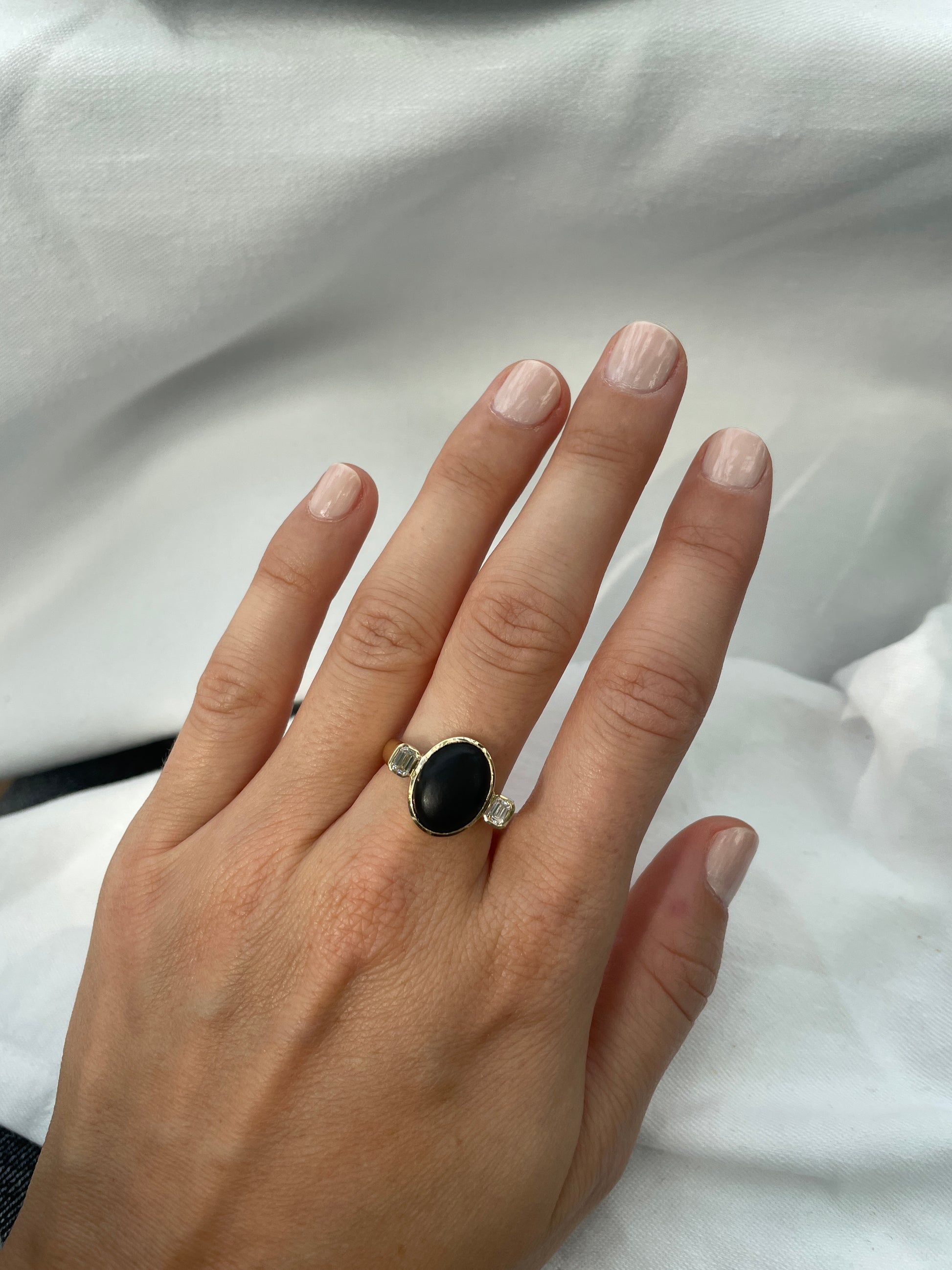 Elegant black onyx ring with emerald diamonds on hand, showcasing a matte finish and round shape for a stylish everyday look.